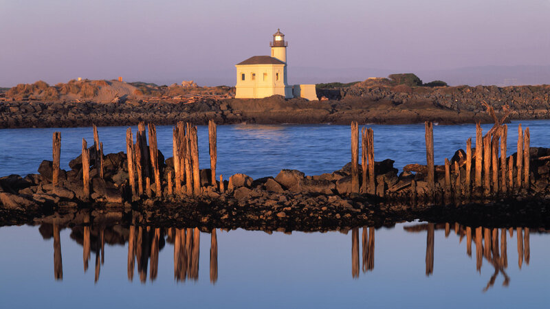Lighthouse on Rocky Shore — Blue, Serene, Sunset, Photograph, Wooden Posts