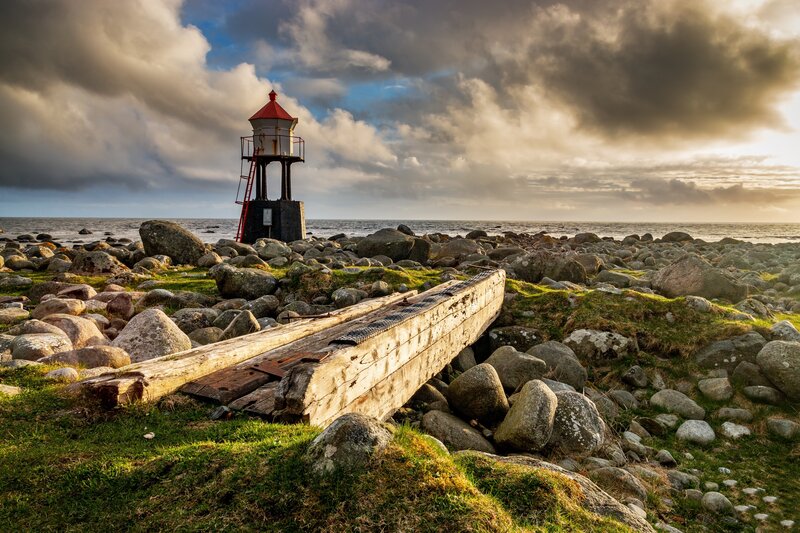 Lighthouse on Rocky Shore — Gray, Dramatic, Sunset, Photograph, Rocks, Wooden Beam