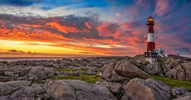 Lighthouse on Rocky Shore — Orange, Dramatic, Sunset, Photograph, Rocks
