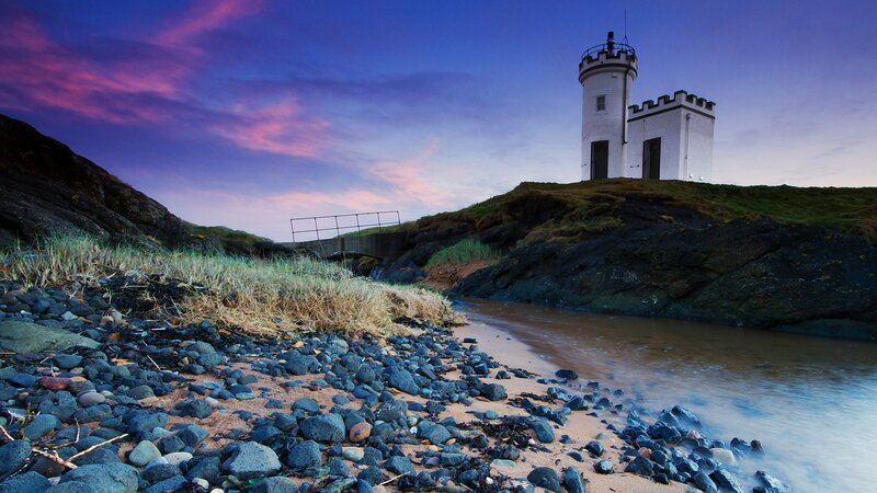 Lighthouse on Rocky Shore — Purple, Serene, Sunset, Photograph, Rocks