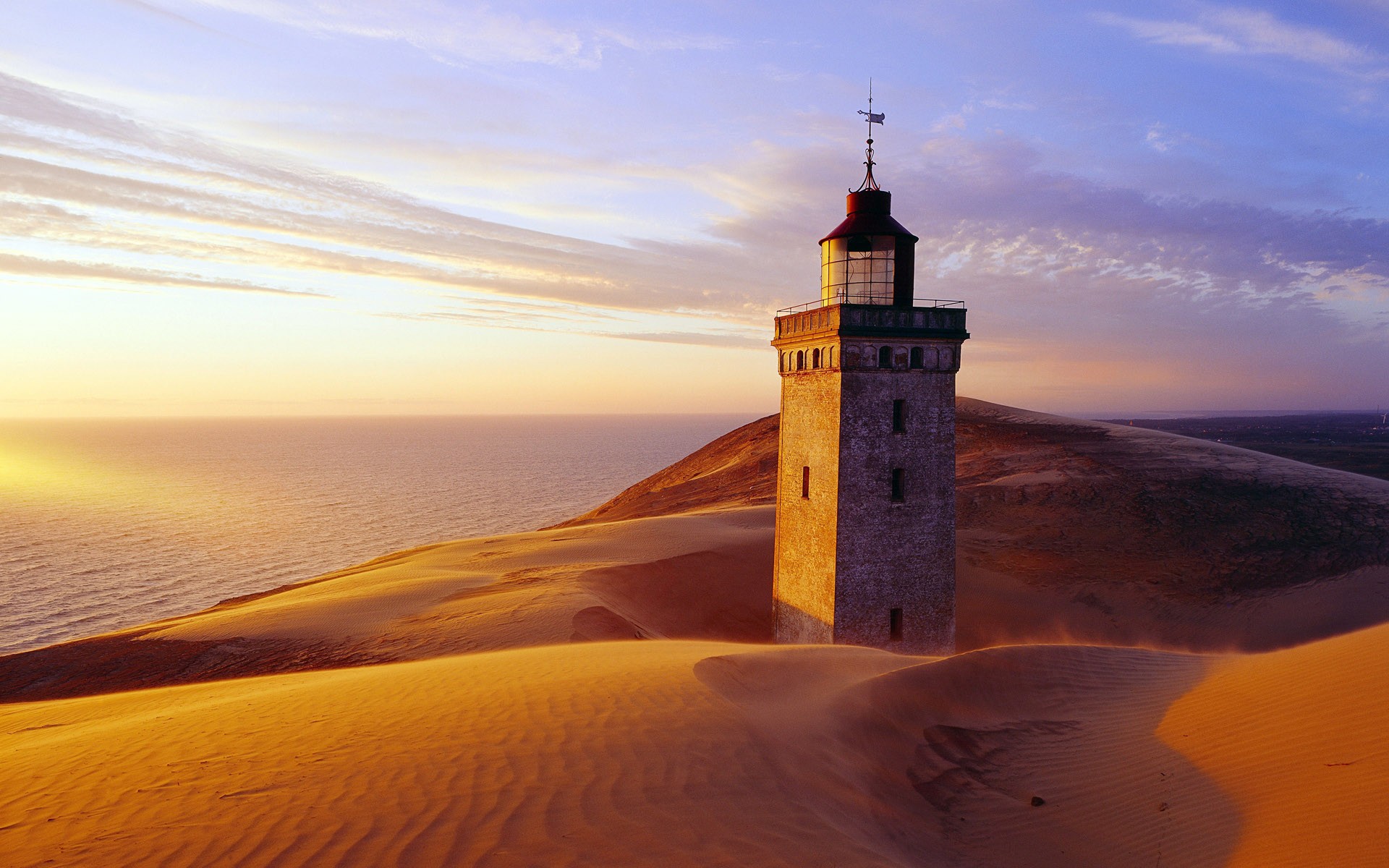 Lighthouse on sand dunes at sunset