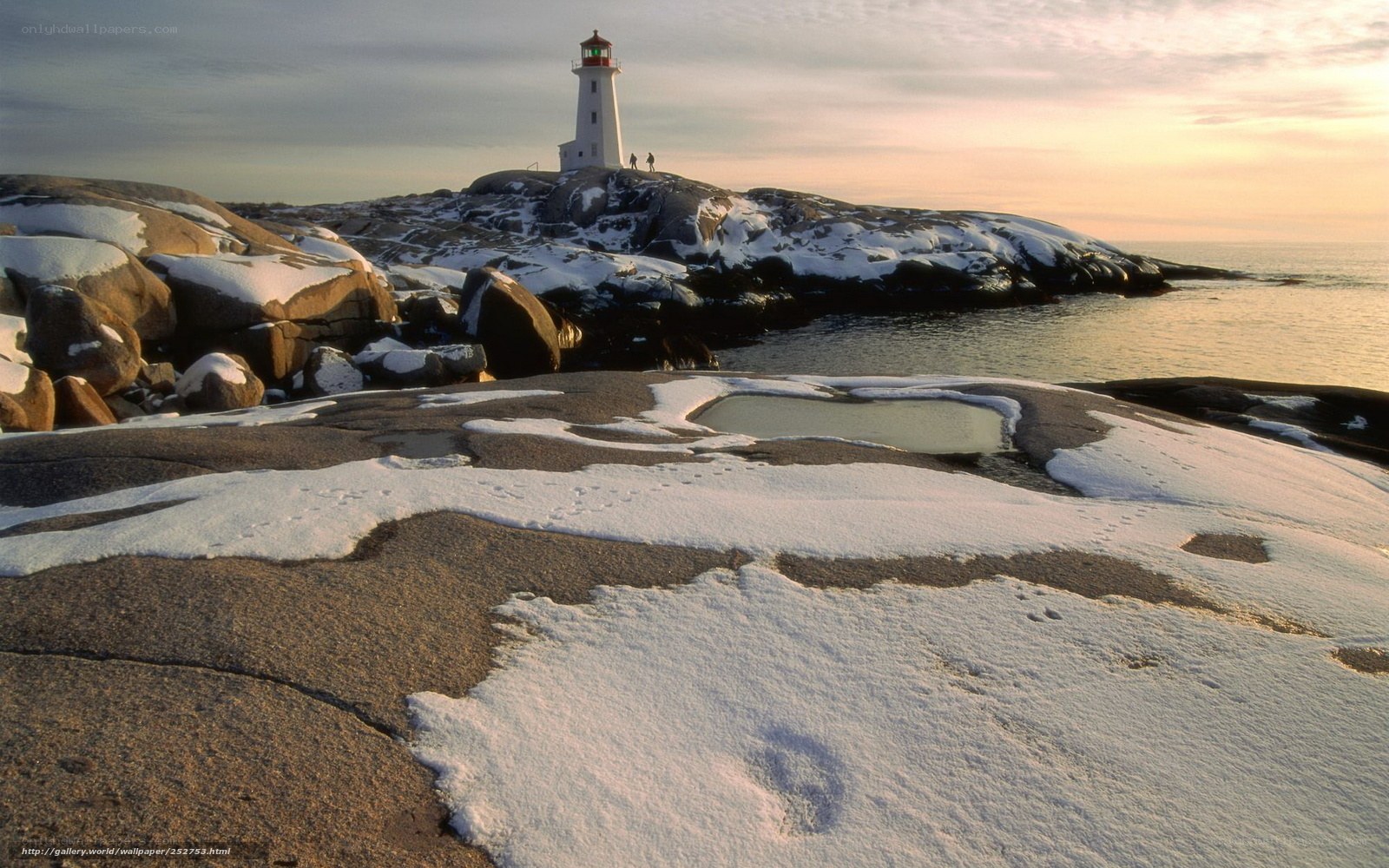 Lighthouse on snowy rocks at sunset