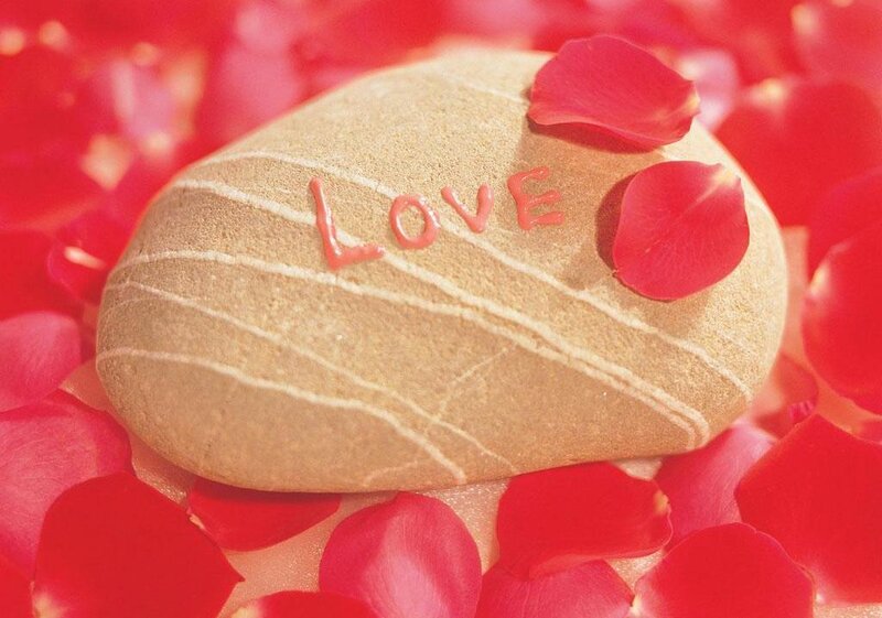 Love carved on a stone with rose petals
