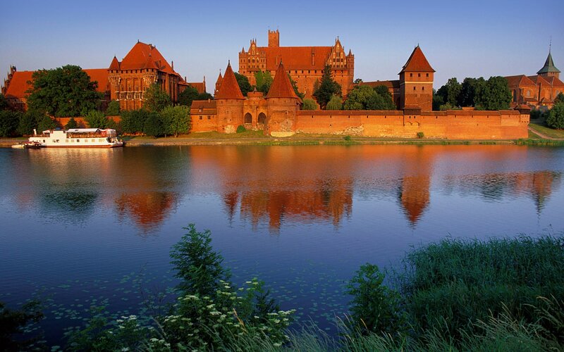 Malbork Castle — Blue, Serene, Sunset, Photograph, River, Boat, Trees, Orange