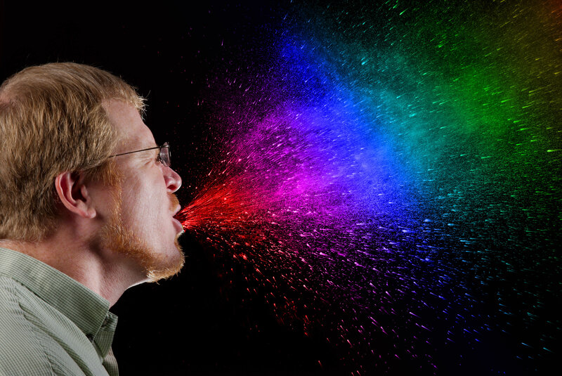 man blowing rainbow spray