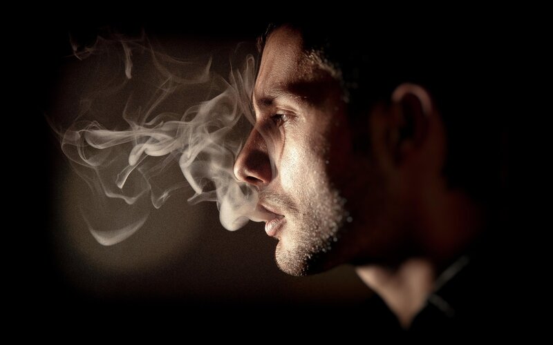 man exhaling smoke in profile