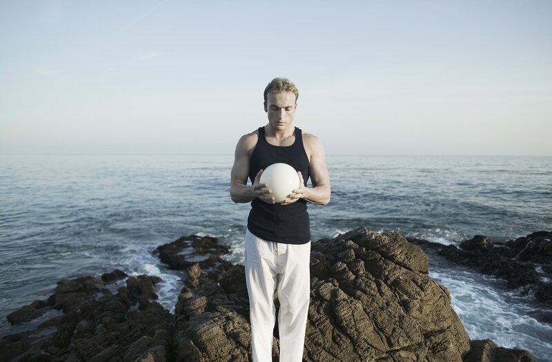 Man holding ball on rocky shore