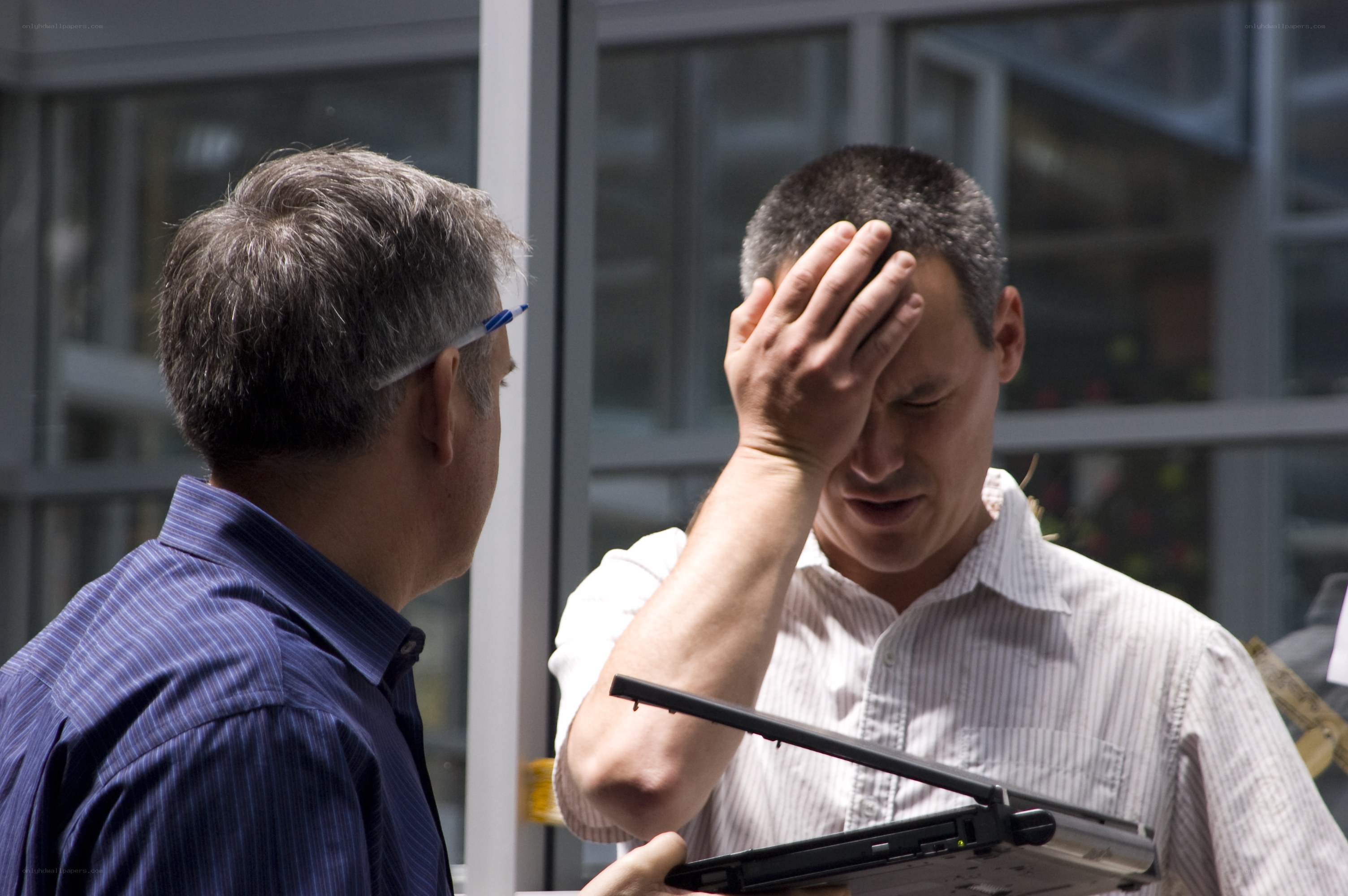 Man holding laptop with hand on forehead