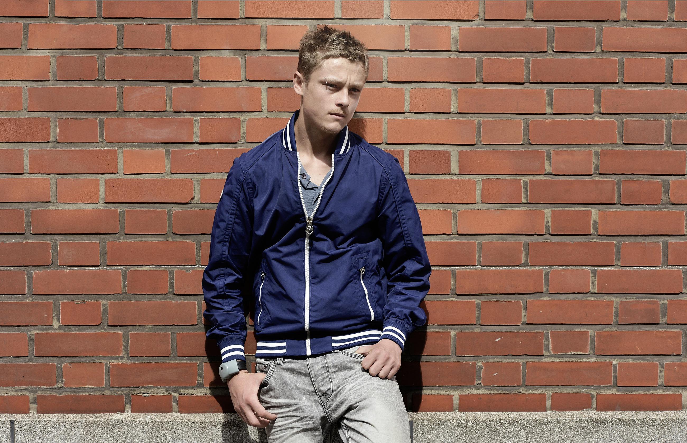Man in blue jacket against brick wall