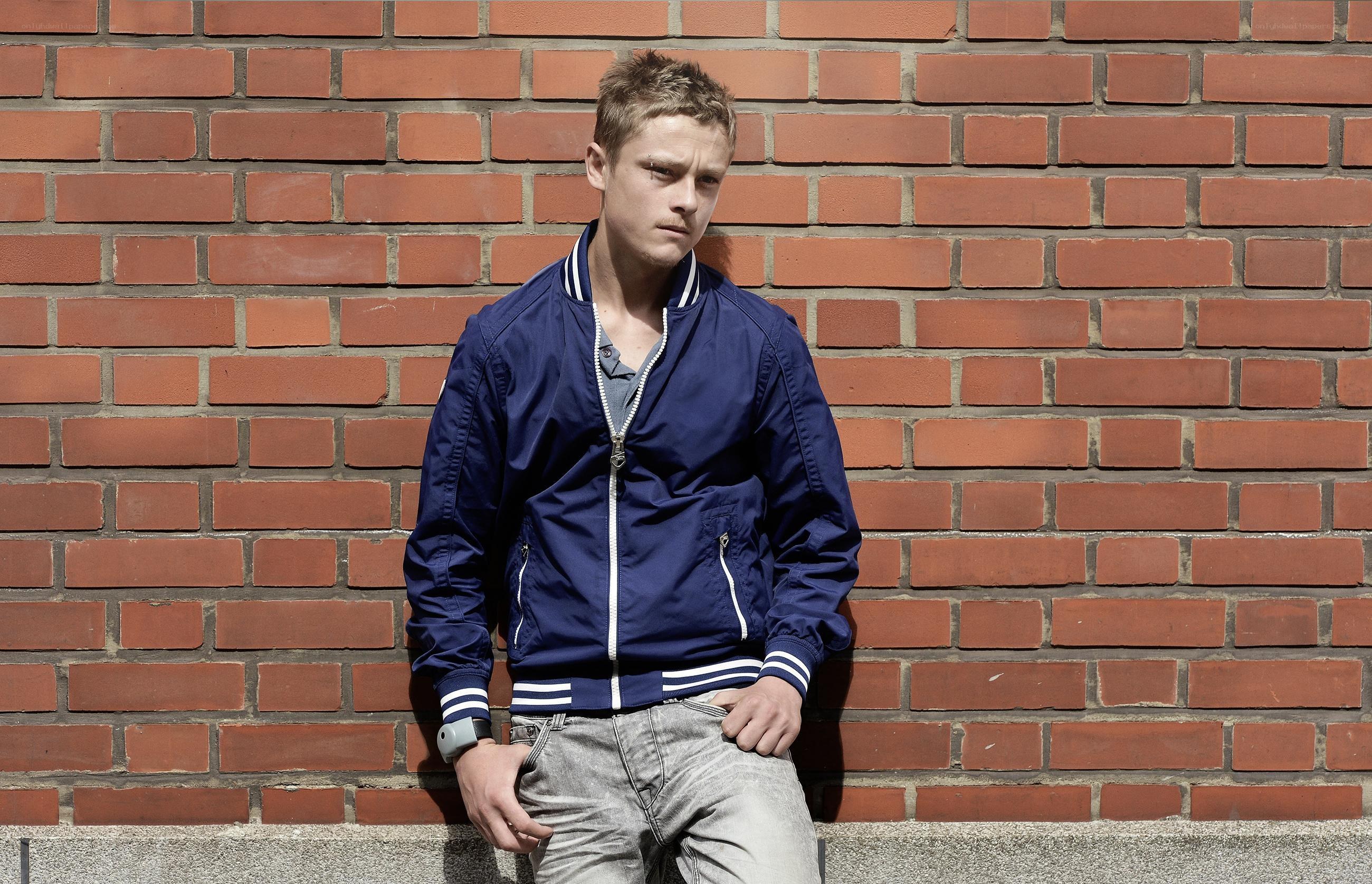Man in blue jacket against brick wall