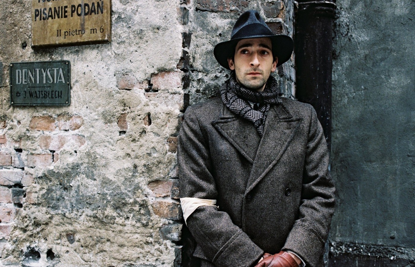 Man in coat and hat by brick wall