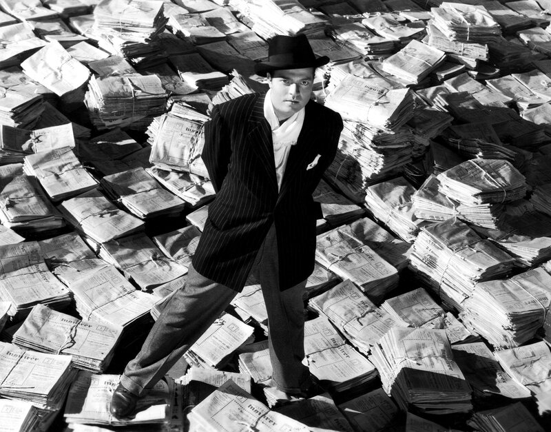 Man in pinstripe suit surrounded by newspapers