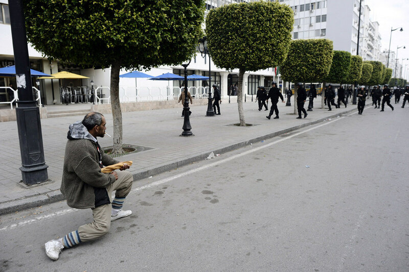 Man kneels as police march