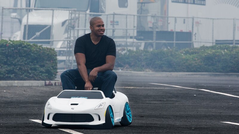 man on toy car in parking lot