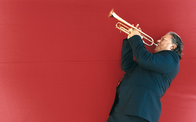 Man playing trumpet against red wall