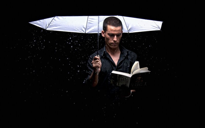 Man reading under umbrella in rain