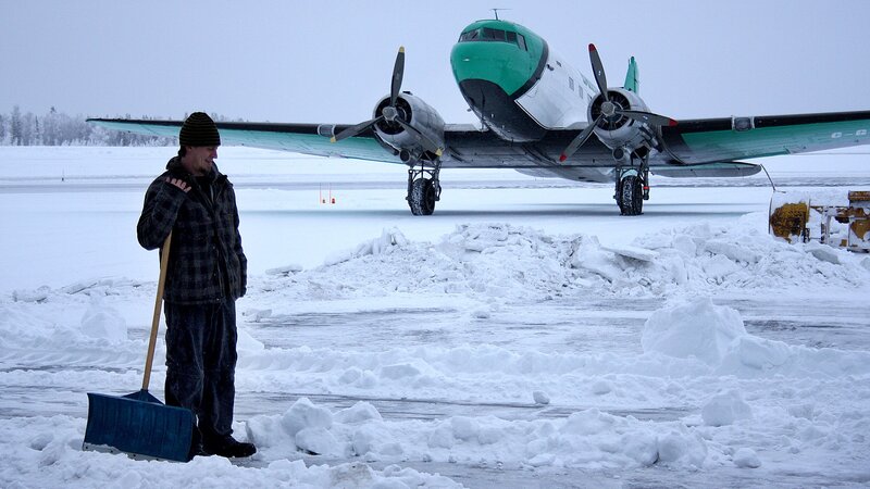 Man shoveling snow near airplane