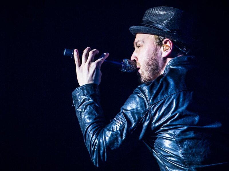 Man Singing into Microphone — Black, Dramatic, Night, Photograph, Hat, Leather Jacket