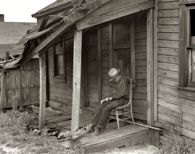 Man sitting on porch of dilapidated house