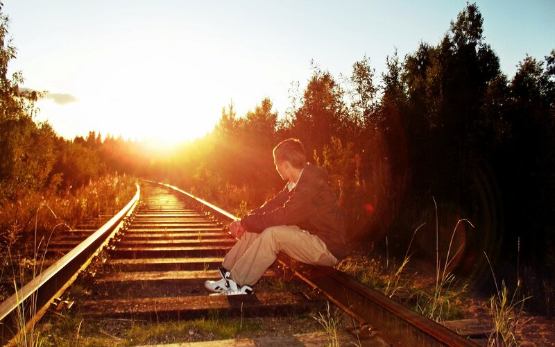 man sitting on train tracks at sunset