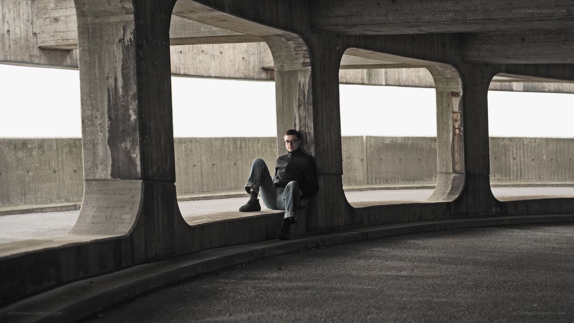 Man sitting under concrete bridge