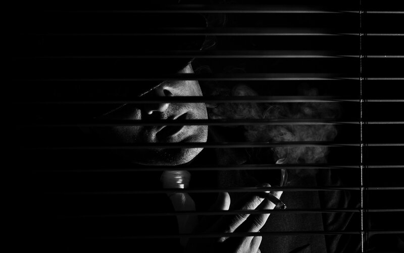 man smoking behind blinds