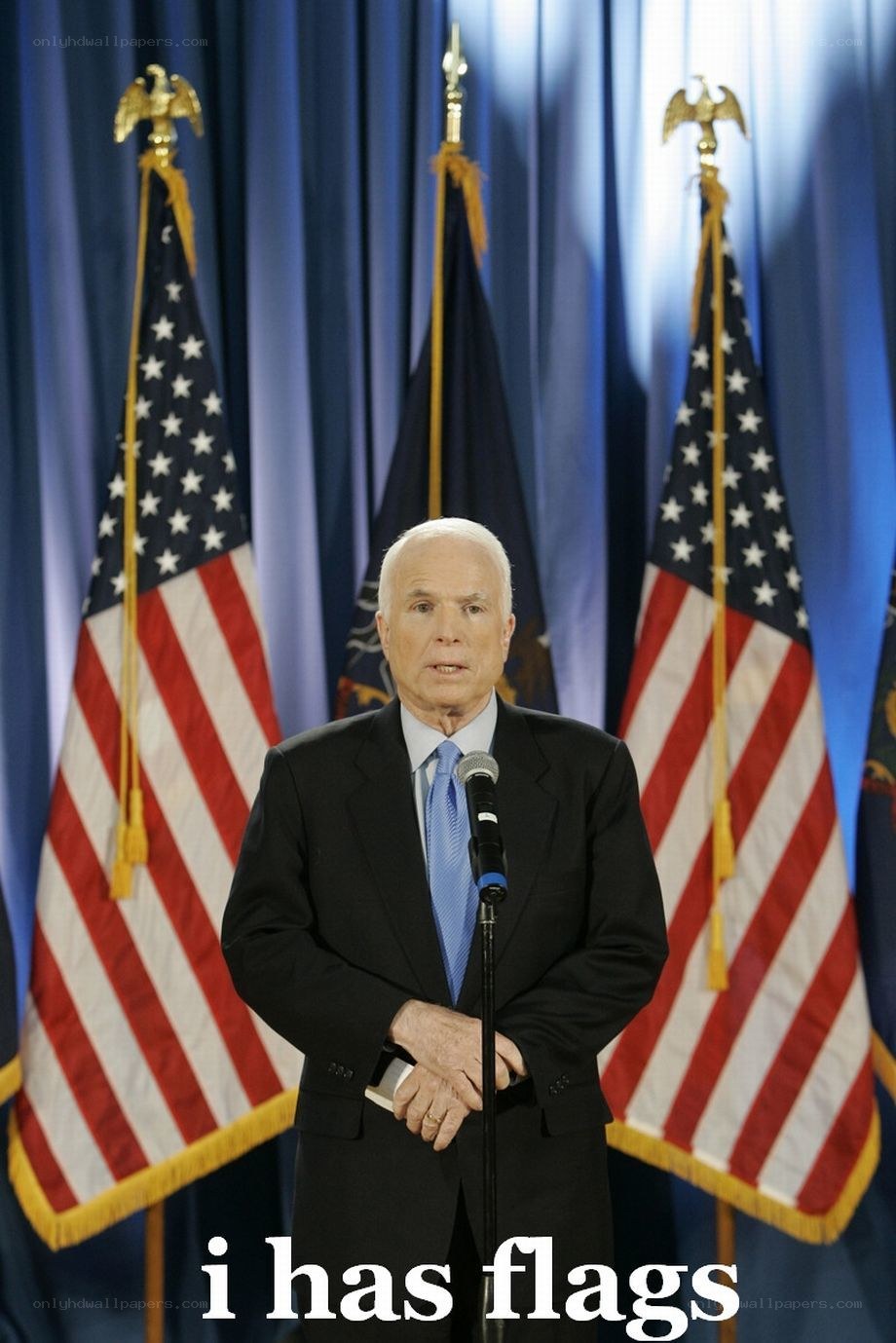 man speaking at podium with flags