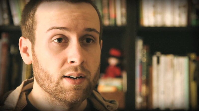 man speaking in front of bookshelf
