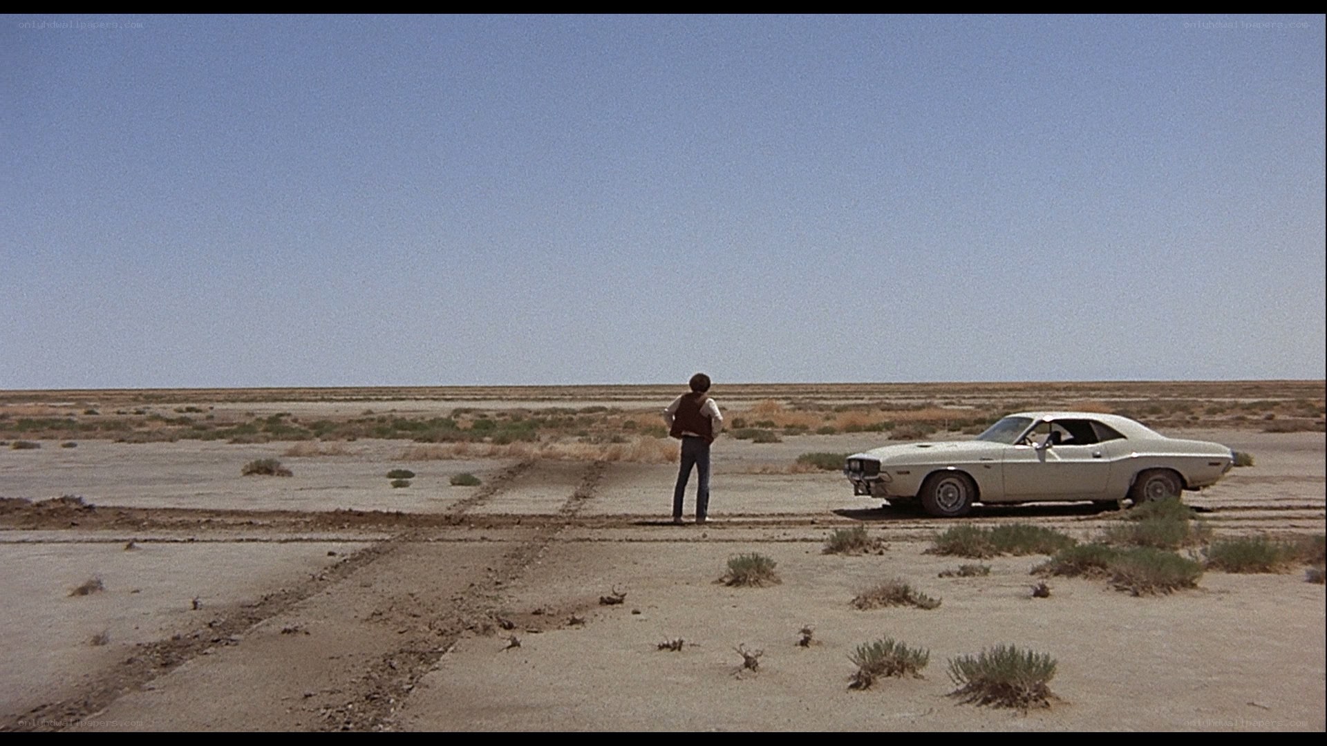 man standing in desert with car