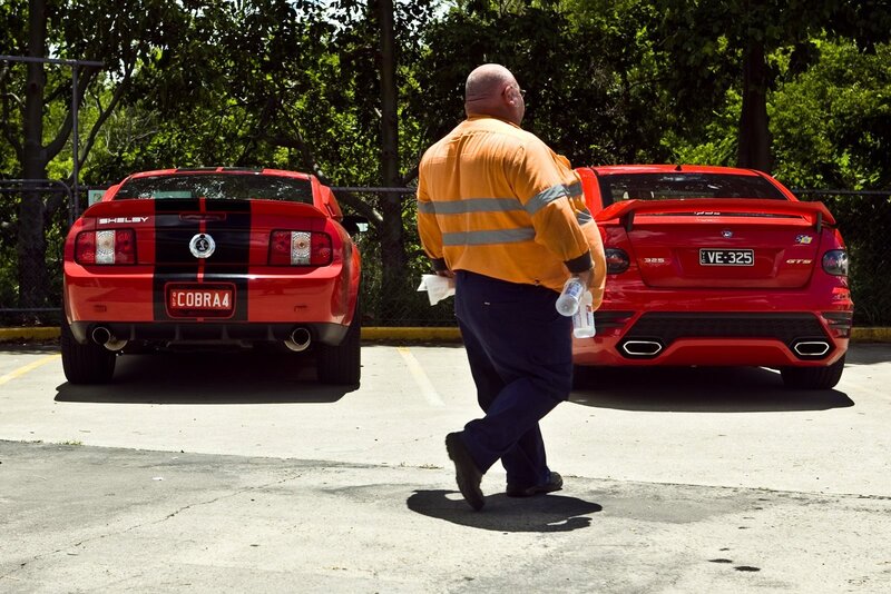 Man walking past two red cars