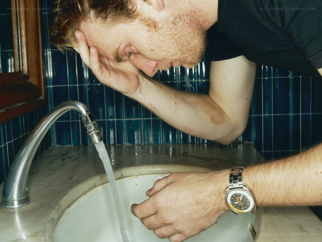 man washing face at sink