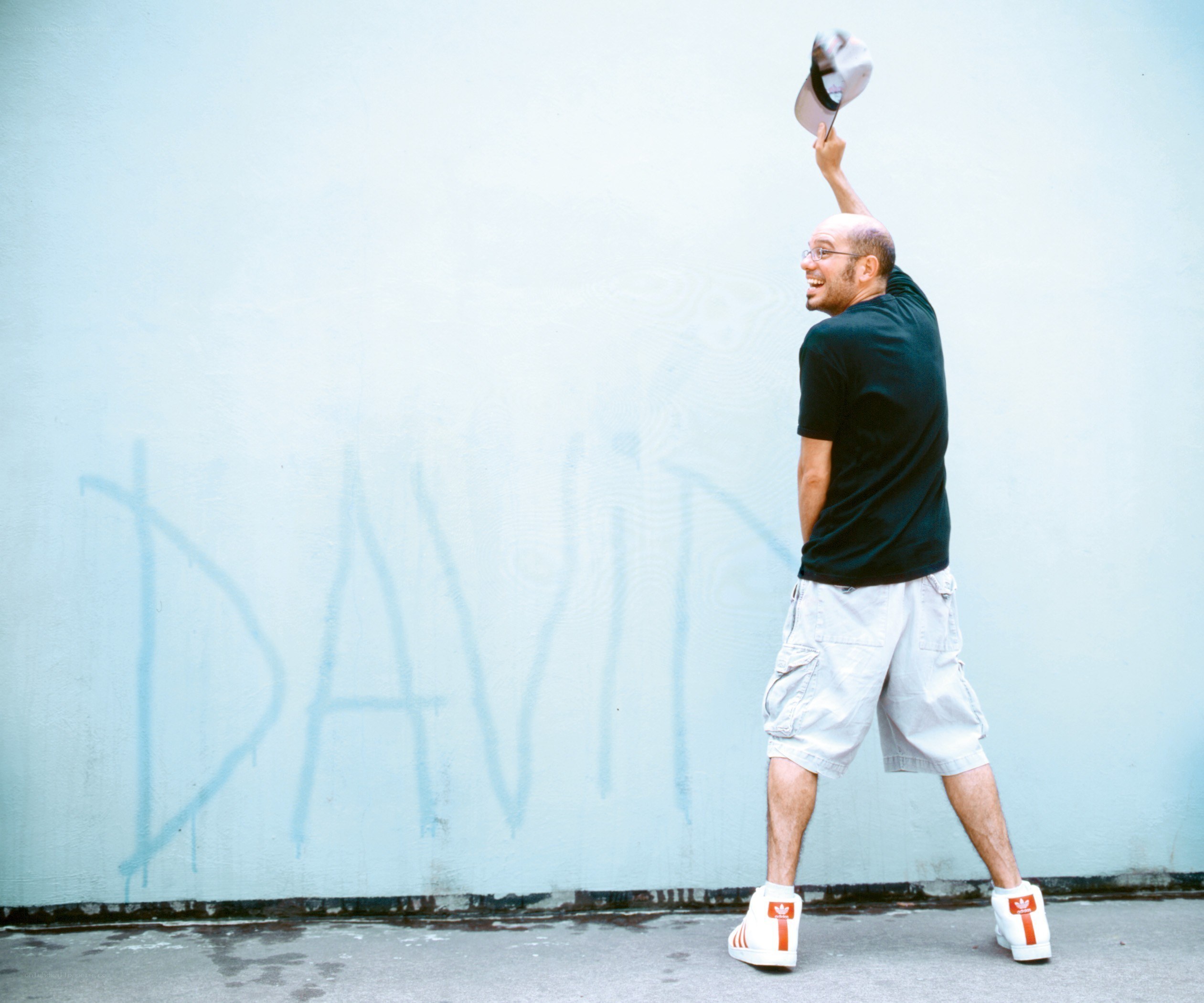 Man waving hat by graffiti wall