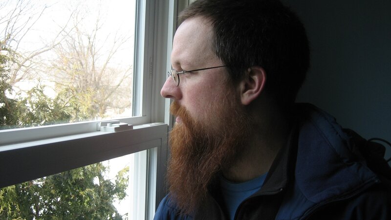 man with beard looking out window