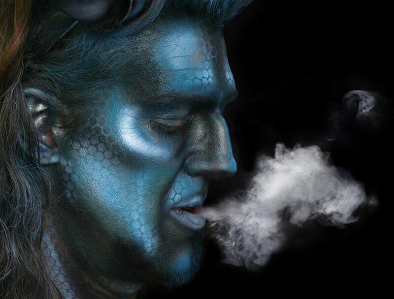 man with blue makeup exhaling smoke