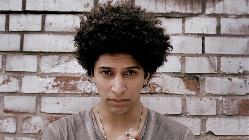 man with curly hair against brick wall