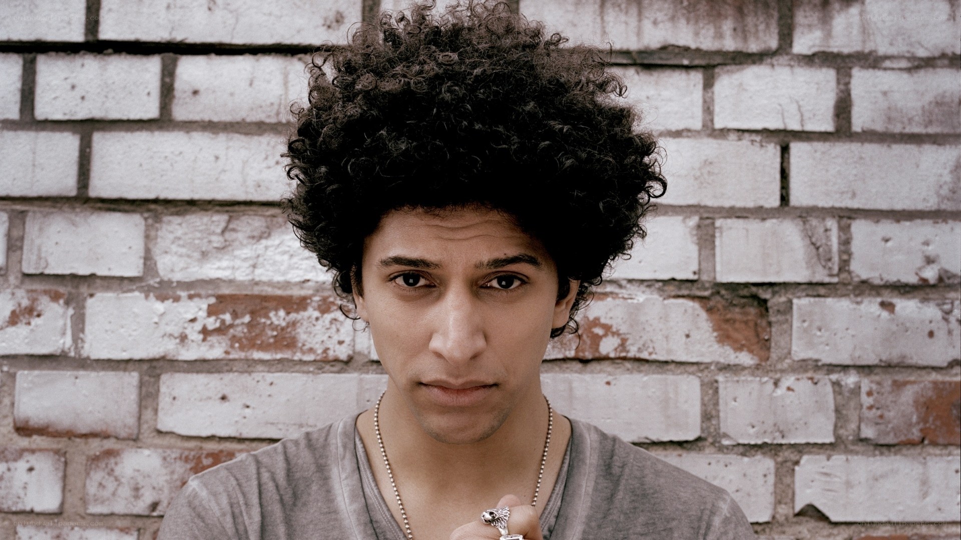 man with curly hair against brick wall