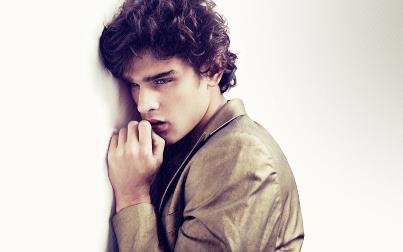 man with curly hair leaning against wall