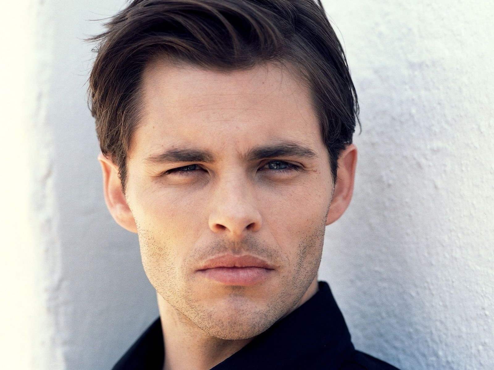 man with dark hair against white wall