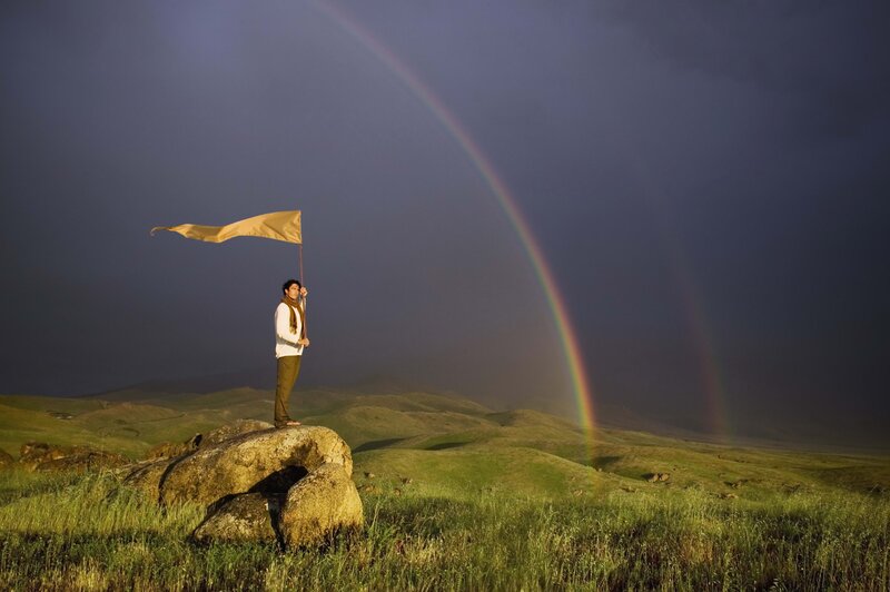Man with flag on hill under rainbow