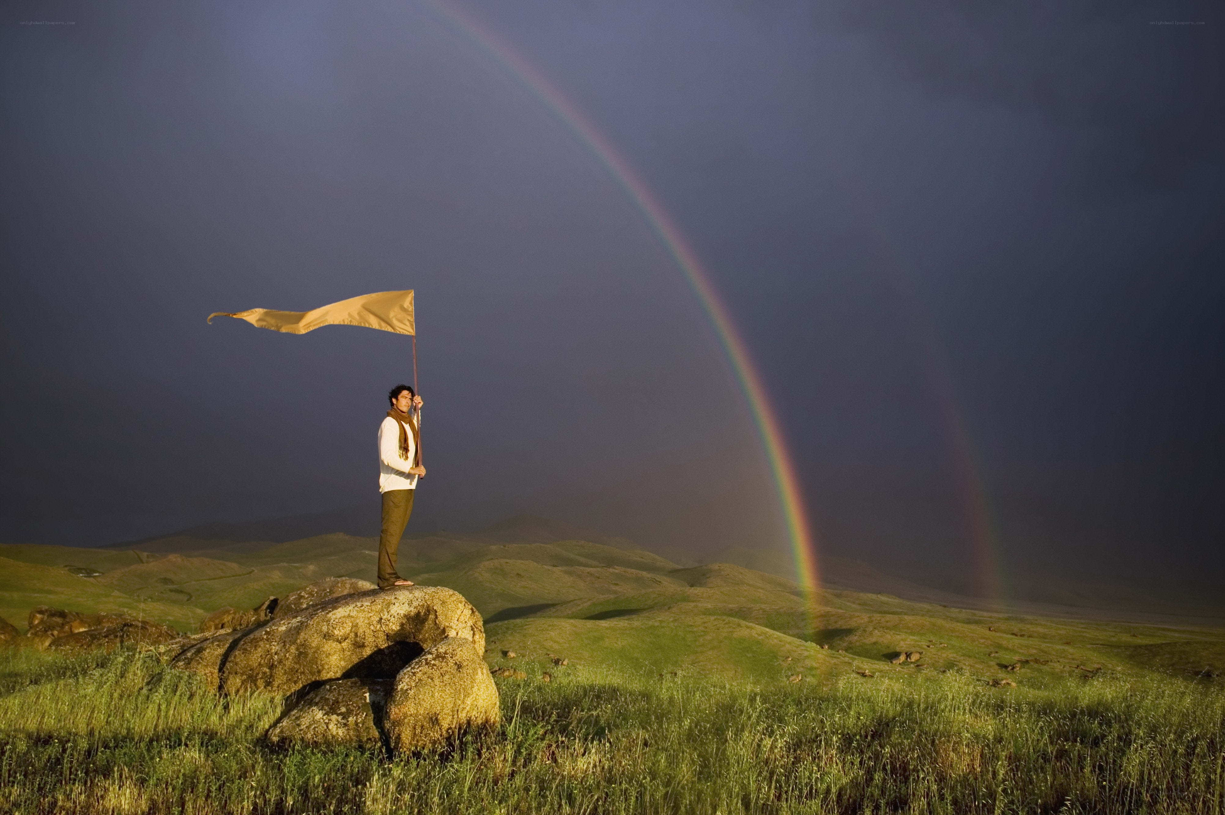 Man with flag on hill under rainbow