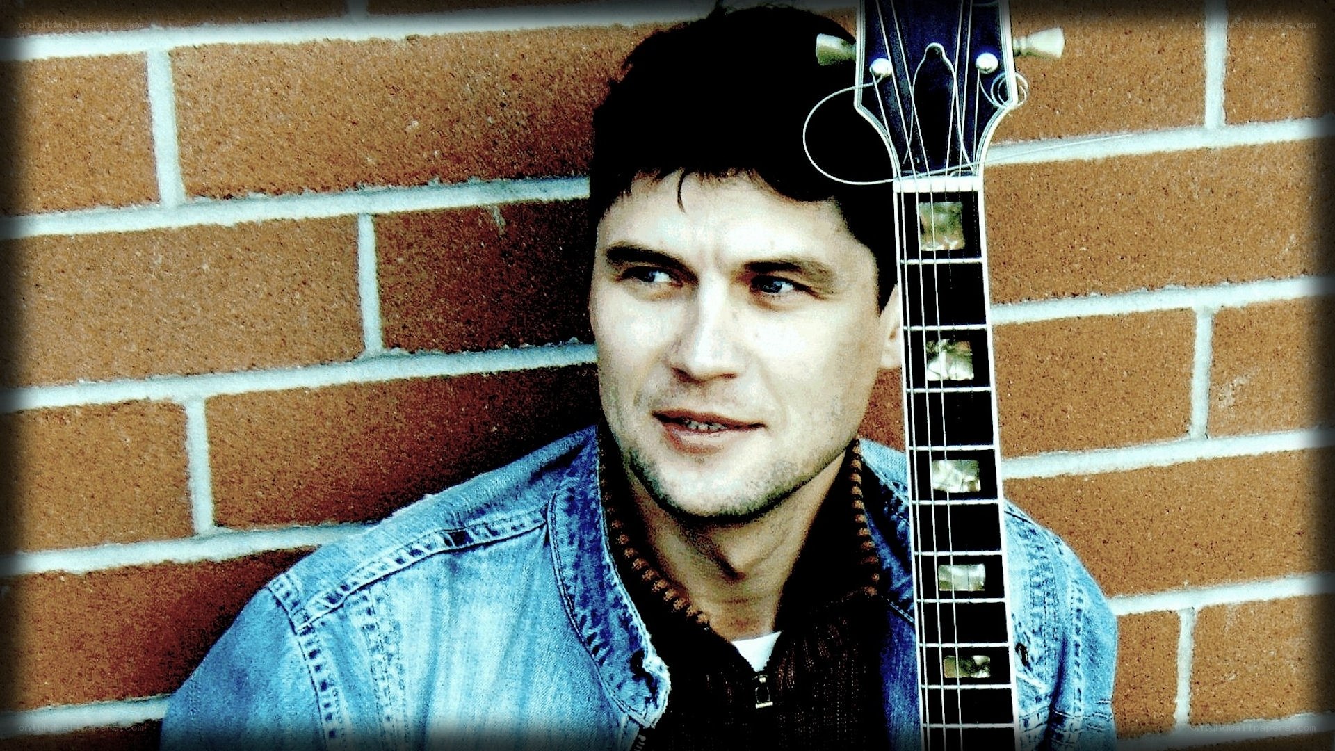 man with guitar against brick wall