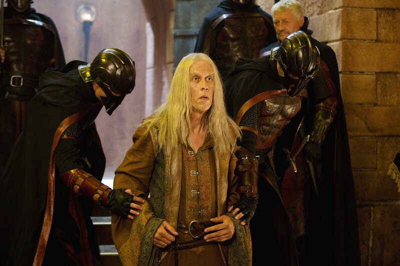 Man with long white hair surrounded by guards
