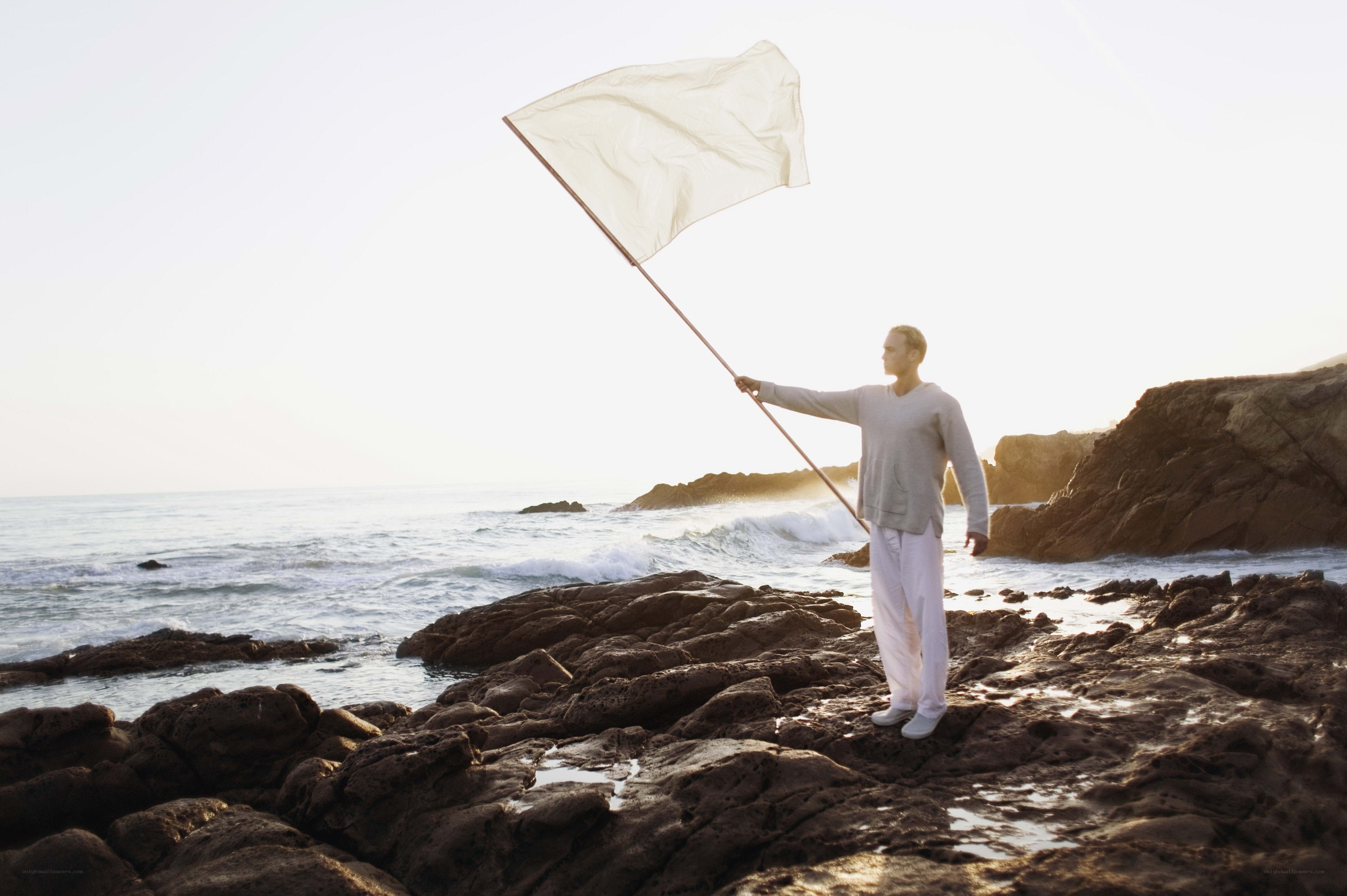 Man with white flag on rocky shore