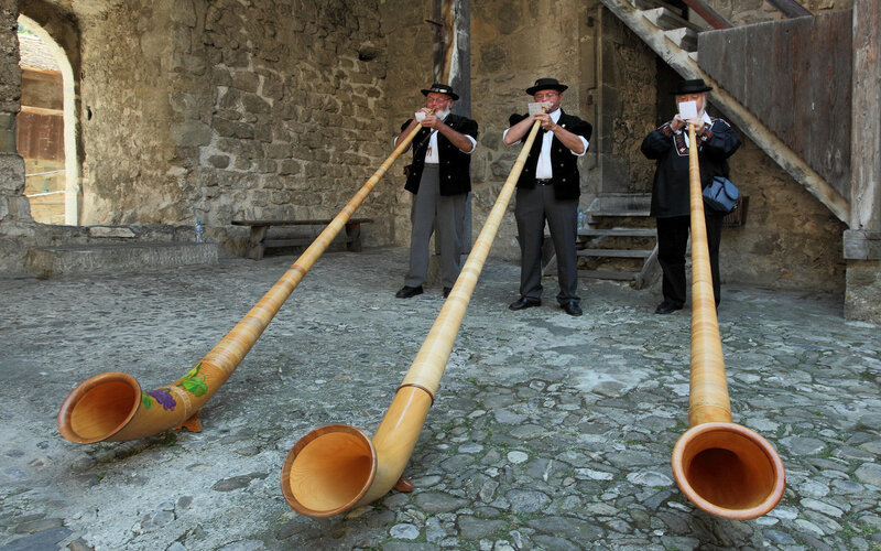 Men playing alphorns in courtyard