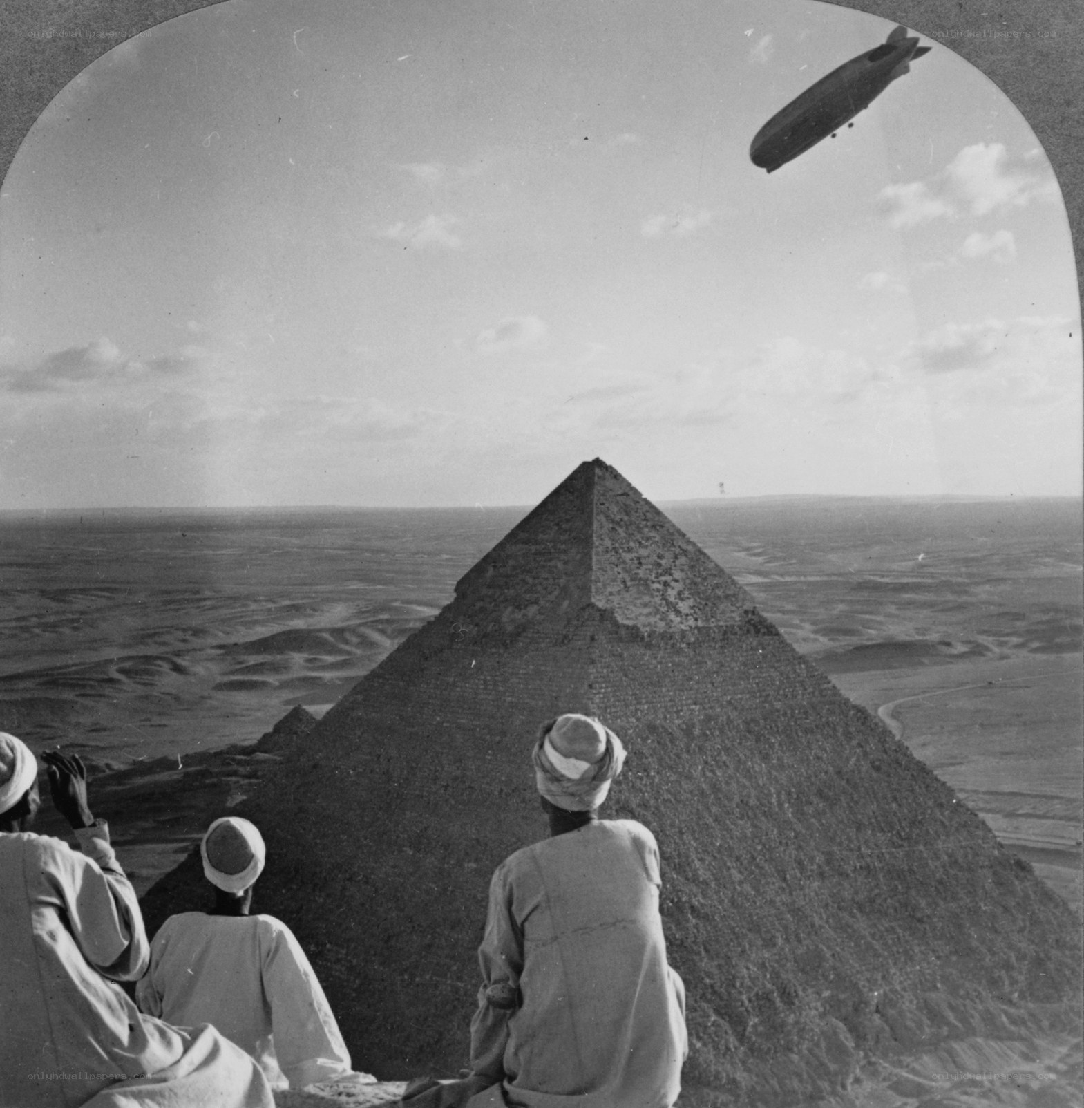 Men watching airship over pyramid