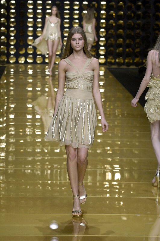 Model walks runway in gold dress