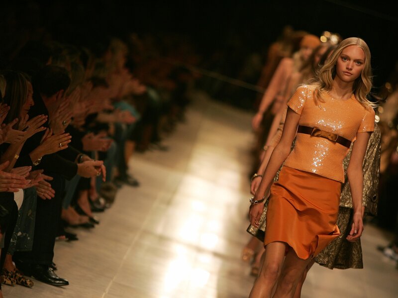 Model walks runway in orange dress