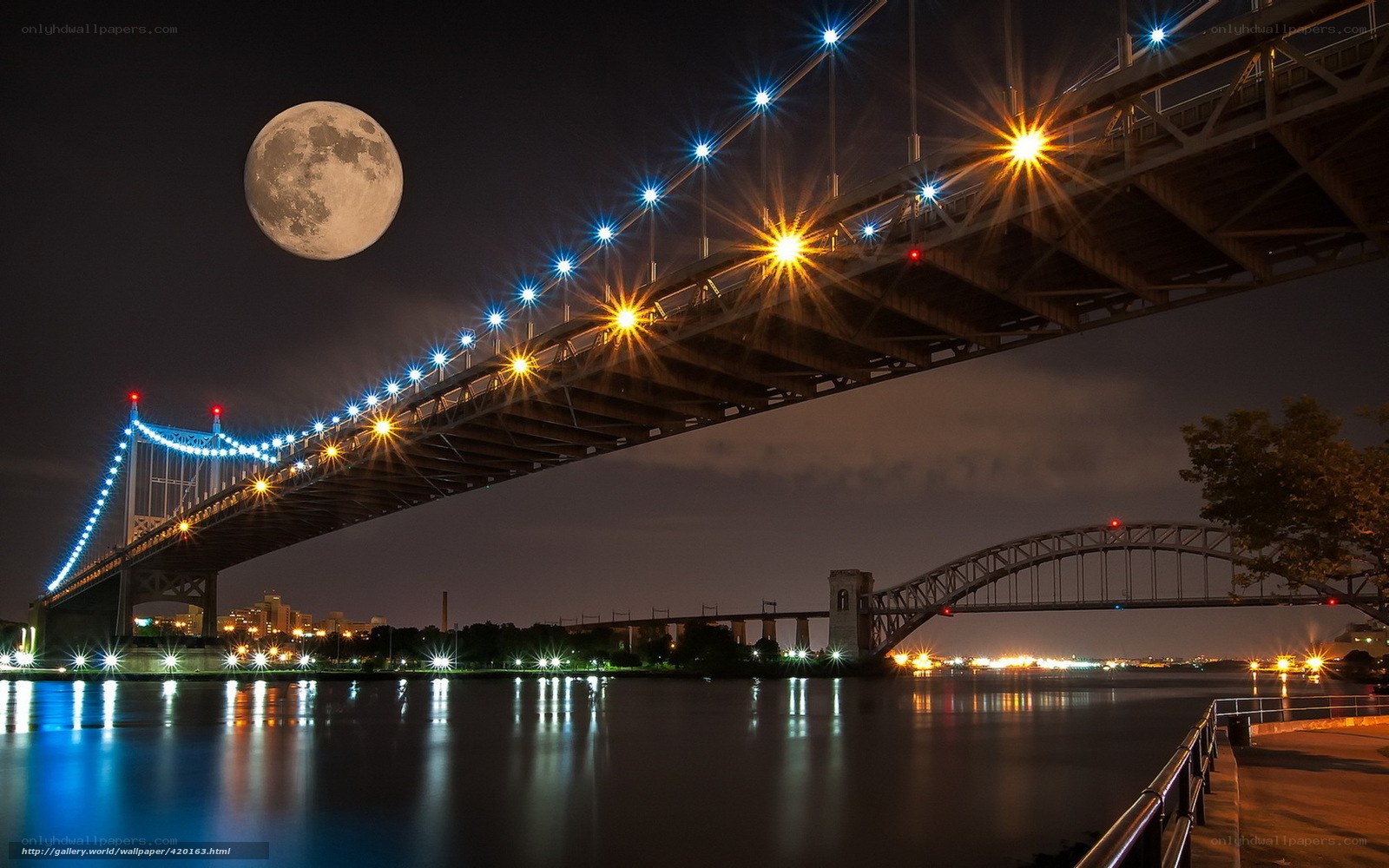 Moon over a lit bridge at night