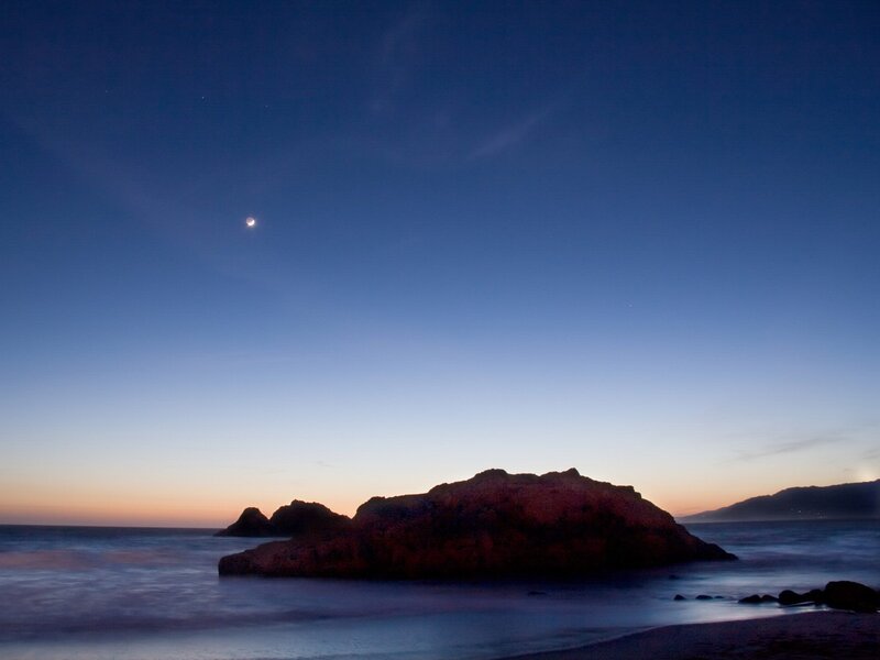 Moon over coastal rocks at dusk