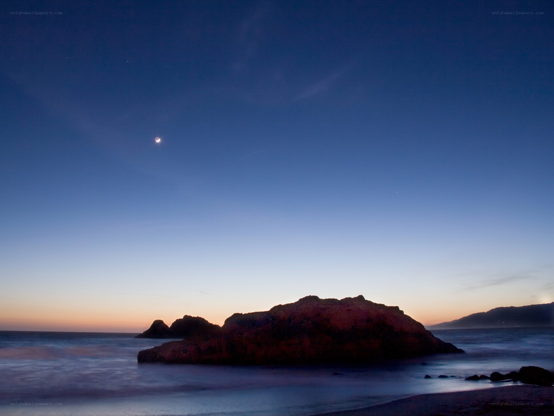 Moon over coastal rocks at dusk